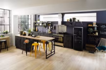 Ambiance semi-industrielle dans cette cuisine " Vega". Avec ses finitions dans deux tons de bois, un "woody dark" foncé pour les façades des meubles et un bois clair pour le plateau, l'îlot central devient tendance. Pratique avec sa partie rangement, l'îlot "table" invite aussi à s'attabler sur la planche sur tréteaux. La touche en plus : des tabourets colorés amènent une touche de fantaisie. A partir de 3254 euros, Cuisinella.