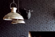 Effet charbon : peint en noir mat, le mur de brique devient chaleureux et profond. Un élément fort de la décoration de l'hôtel Rooms, perdu au milieu des montagnes du Caucase. Design, agence Rooms. Lustre en métal martelé, Flamant.