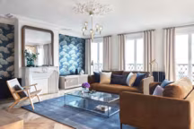 Afin de préserver une certaine cohérence, Lichelle Silvestry choisit le mobilier du salon proportionnel à l'espace, assez généreux. Un canapé moelleux et accueillant est complété par un fauteuil chaleureux et une assise ethnique. Autour d'une table basse en verre design, l'ensemble est singulier. Au sol, un large tapis est un joli clin d'œil à la couleur présente sur le mur. Et au plafond, une suspension contemporaine contraste avec les moulures d'origine.
(canapé et fauteuil Oscar AM.PM, table basse Sybil AM.PM, suspension Ledo Hubsch, tapis Eberling AM.PM)