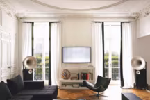 Dans le salon, donnant sur le Jardin des Tuileries, les portes-fenêtres sont habillées de rideaux en taffetas gansés de larges bordures noires. Sur le meuble bas laqué blanc, une lampe en verre de Murano ainsi qu'une sélection de livres de mode et d'art. De part et d'autre, des haut-parleurs "Duo Grosso", Avantgarde Acoustic. Fonctionnel, un canapé d'angle capitonné en coton et laine et un fauteuil de relaxation, le tout, BoConcept. La table basse et le banc ont été dessinés sur mesure par Magdalena.