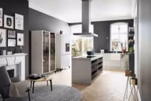 Ilot central composé de tiroirs ouverts offrant une visibilité et un accès pratique aux ustensiles. Sur le dessus de l'ilot se trouve la plaque de cuisson intégrée avec une hotte suspendue au plafond. Plan de travail en composite moucheté, coloris bianco river, tiroirs en stratifié effet bois et finitions latix terra, panneaux latéraux brillant en similaque, ton gris sterling, prix sur demande, SieMatic.