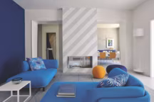 Dans le salon spacieux et convivial, tout tourne autour de la cheminée zébrée de lignes grises comme une ombre venue de l'extérieur : deux sofas Peg en laine légère dessinés par Nendo pour Cappellini, tapis Dot (Hay), luminaire mural Soft Spun Large de Sebastian Wrong (Flos) et poufs boules Tato et Tatino (Baleri Italia). Au fond à droite, dans la salle à manger, chaises blanches Baleri Italia. A gauche, la porte ouverte sur le vestiaire d'amis laisse deviner un jeu graphique pictural de lignes noir et blanc.