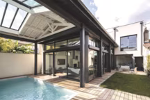 Ouverte par de grandes baies coulissantes, cette véranda est abritée par une toiture à isolation renforcée, qui protège également la piscine. Modèle Eden+, Sapa