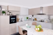 Nouvelle cuisine Genova/Aosta, design made in Italie, laque mate pour le programme Genova, façade avec poignées, caissons blancs, mélaminé structurée pour le programme Aosta, plan de travail stratifié marbre de Carrare avec cuve intégrée de manière semi affleurante sous le plan de travail, coin snack. Prix selon composition. Darty Cuisine