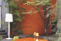 Terrasse vitaminé. Le mur peint ("XPro3 Façade 2 en 1", teinte orange millet, Ripolin) égaie cette cour parisienne réalisée par Sabz. Table "Zonda", Matière grise ; chaises "Myto", Plank ; lampadaire "Inout", Metalarte.