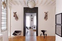 Ci-contre, l'entrée s'ouvresur une géométrie en noir et blanc d'une grande rigueur. Trophées de zèbres, suspension "Snowball" de Poul Henningsen, Louis Poulsen. Fauteuil "Butterfly" de Pierre Paulin et chaise "PKO" de Poul Kjærholm. Tableaux "21186" de Micka, galerie Mark Hachem. Dans le salon, trophée d'onyx, suspension "Artichaut" de Poul Henningsen, Louis Poulsen ; canapé "Kilt" par Emaf Progetti, Zanotta. Fauteuil "PK22" de Poul Kjaerholm, Fritz Hansen.
