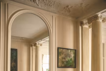 Le salon haussmannien est orné de colonnes néoclassiques. Sur la cheminée, une sculpture en plâtre d'atelier 1930-40 chinée, à droite, un pastel de Piero Ruggeri. A côté de la table en marbre de Gae Aulenti, un repose-pieds vert de Matteo Grassi.