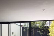 La cuisine, à l'extrémité du loft, jouit d'un second patio agencé par le paysagiste Grégorie Fieux, de Caracterre. Tabourets de bar en fil d'acier " Bertoia » d'Henri Bertoia, Knoll, cuisine laquée gris perle réalisée sur mesure et plan de travail, Corian® Designer White.