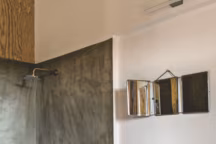 Dans une maison en Corse, cette salle d'eau a été pensée de façon simple et économique, en collaboration avec l'architecte d'intérieur Véronique Lecomte. Des matériaux originaux sont détournés de leur usage initial. Le meuble vasque est fabriqué avec des planches de coffrage à béton ; le sol et les parois murales de la douche sont enduits de colle à carrelage et couverts d'un vernis hydrofuge