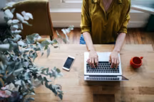Overhead image of a female novelist, blogger, freelancer or a photographer, typing on the laptop keyboard in her living room in the beautiful bright apartment in Paris city center, in Montmartre district. She has a nice wooden retro table and a matching, vintage wooden floor. Retro processed with vibrant colors. Fashionable blogger, freelancer, work from home concepts in a laid back, cozy atmosphere in Paris, France.
