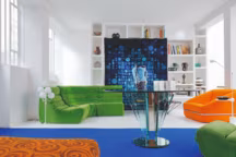 Dans le fond, un tapis, Desso, Hollande 1970, s'expose comme une tenture murale sur la bibliothèque où l'on retrouve différentes céramiques des années 1950, comme celle sur la table en verre attribuée à Pietro Chiesa, Fontana Arte, 1970. Au pied du sofa modulable en velours vert côtelé, non attribué, France 1970, lampe avec sept boules en opaline de Kaiser Lutschen, Allemagne 1950, à droite, fauteuil orange à structure chromée, non attribué, Italie 1970, et petite table postmoderne, Edward Geluk, Arco, 1980.