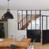 Avec une cloison façon verrière, les espaces communiquent pour une lumière naturelle optimale. Si la verrière est conçue avec une porte battante, elle s'ouvre d'une pièce à l'autre. Une cloison avec un soubassement stylée pour une maison à l'esprit atelier. 
Plus d'infos : porte battante Créative en acier, vitrage transparent Saint-Gobain feuilleté sécurité des personnes 33.2, finition thermolaquée noir satiné, prête à poser en dimensions standard ou sur mesure, pose en tunnel, avec éléments complémentaires, à partir de 999 euros, Lapeyre.