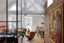 Le charme d'une soupente rendue à la lumière, posée comme un nid dans la charpente. De part et d'autre de la fenêtre, bibliothèques dessinées par Stéphane Poux et laquées orange. Table basse et canapés signés Intérieur Design. Lampadaire " Ion » et coussins, Caravane. Fauteuil " Lounge Chair » de Charles et Ray Eames, Vitra chez The Conran Shop. Sur le mur d'entrée, tapissé d'un papier en paille naturelle " Antilles Weave », Thibaut chez Au Fil des Couleurs, toile de Mick Micheyl. La verrière réalisée par Inox.fr sépare la cuisine de la pièce.