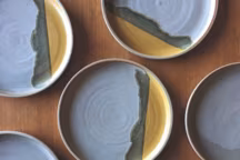 Assiettes en grès de Saint-Amand de la collection Odyssée, réalisée par Marine Feuillerat, aux nuances de gris mat, ocre satiné et gris-vert obtenu par mélange après cuisson, des couleurs inspirées par la nature landaise environnante ; uniques et poétiques, elles vont au lave-vaisselle et au micro-ondes.