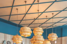 Tables au plateau de pierre de lave, banquettes en cuir, canapés et chaises recouverts de velours, tapis et suspensions en verre de chez Maison Sarah Lavoine, luminaires en rotin " Antibes » par Currey & Company.