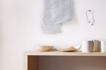 Toute la beauté de la collection " Hagire ». Au mur, collier " HN-02C », et, sur le buffet, bols, assiettes carrées et tasses avec anse, effet lin et coton à motifs carrés.