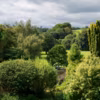 Vue sur la vallée et sa rivière bordée de saules, de peupliers, de chênes verts, ou Quercus ilex ; statue de bronze romaine et, au premier plan, des Clerodendrum trichotomum et Taxus baccata (ifs).