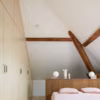Chambre mansardée avec une tête de lit en bois foncé. Réalisation HEJU Studio