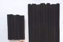 Derrière elle, deux sculptures murales grand format de la série " Lanzarote ». Le carton est travaillé en volume et recouvert de peinture noire mate projetée à haute pression. Au sol à droite, une pièce de la série " Polaire », carton, patine au blanc de Meudon.